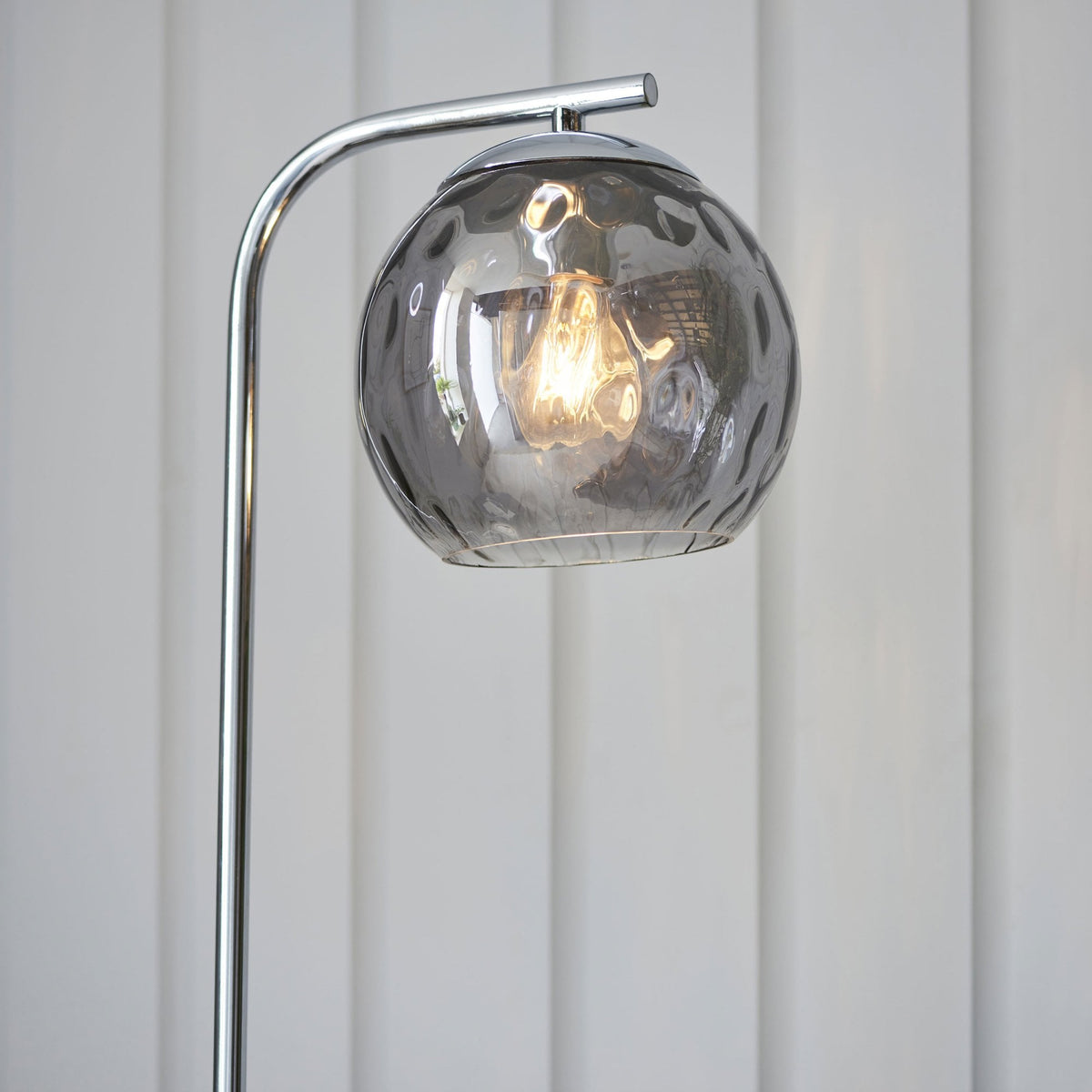 Close-up of the smoked glass shade of a chrome floor lamp, showing the textured glass and warm light.