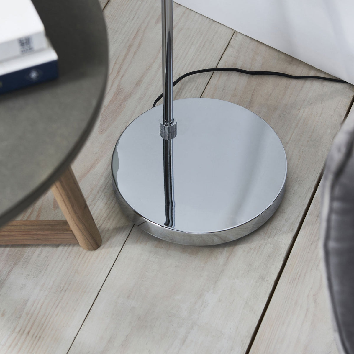 Close-up of the round, polished chrome base of a floor lamp on a light wooden floor.
