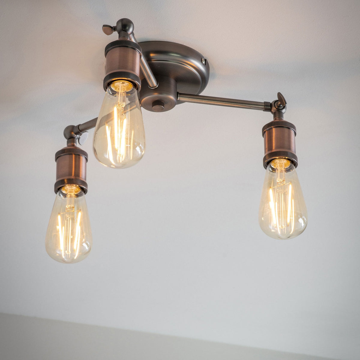 Three-light semi-flush ceiling light with antique copper bulb holders and exposed bulbs.