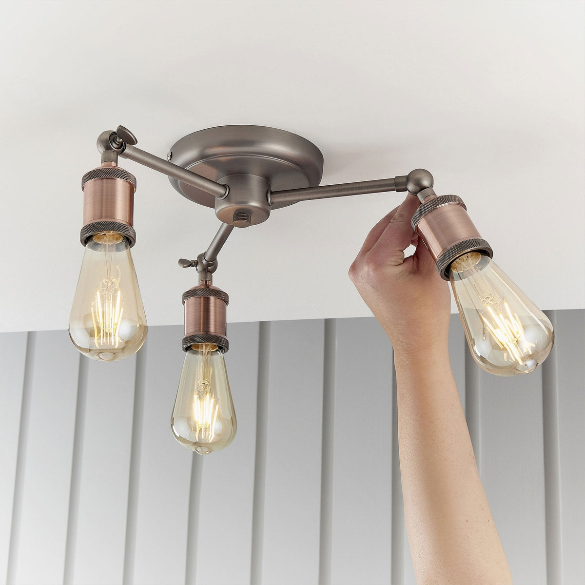 Hand adjusting one of the three lights on a semi-flush ceiling fixture with antique copper bulb holders.