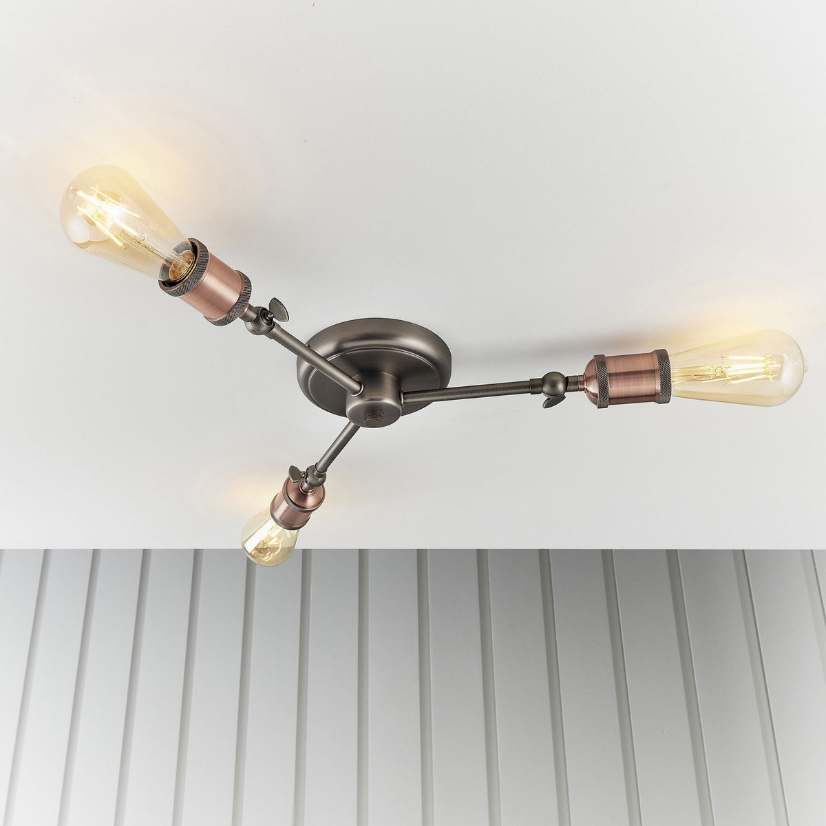 Three-light semi-flush ceiling fixture with antique copper bulb holders, two lights angled upwards.