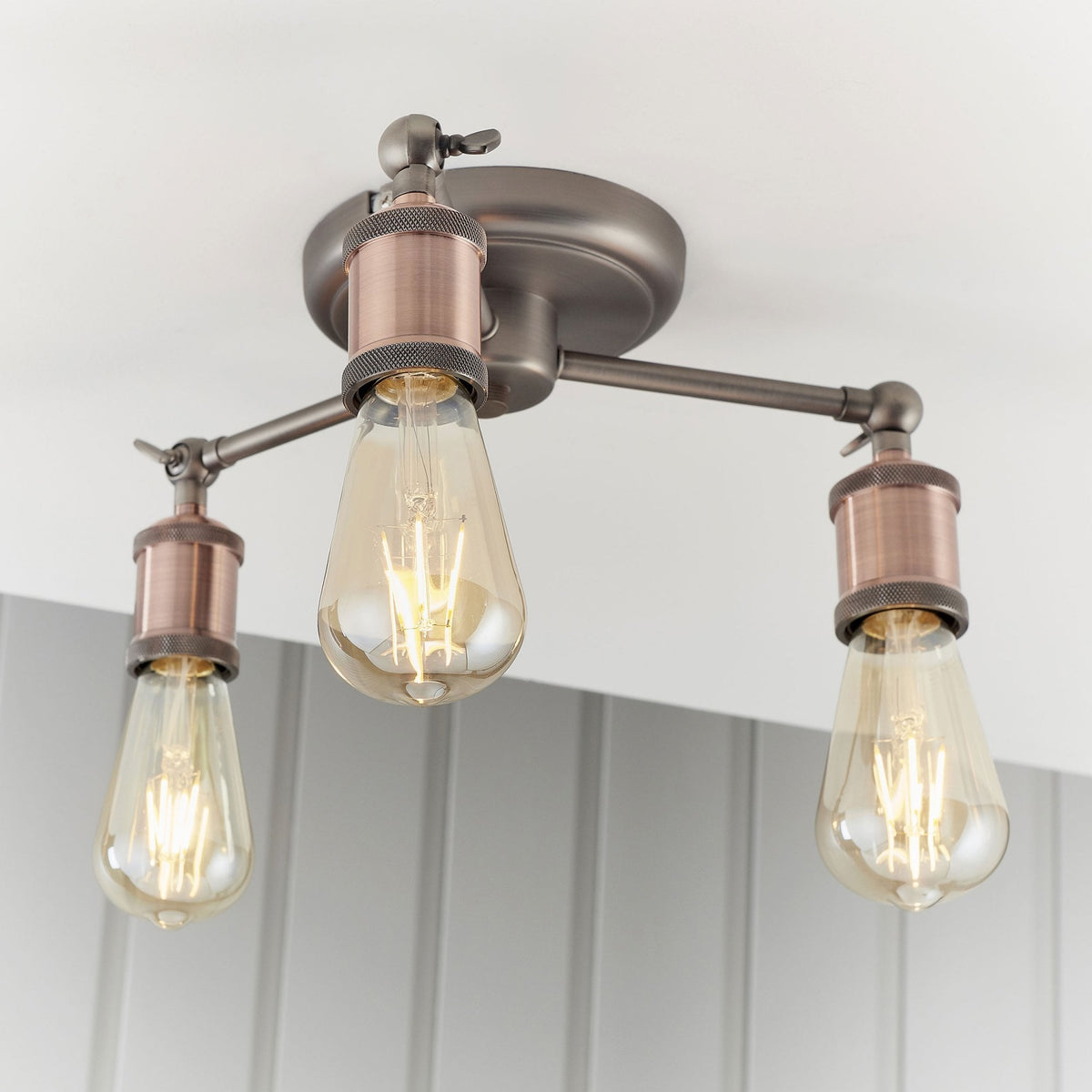 Close-up of a three-light semi-flush ceiling fixture with antique copper bulb holders and exposed bulbs.