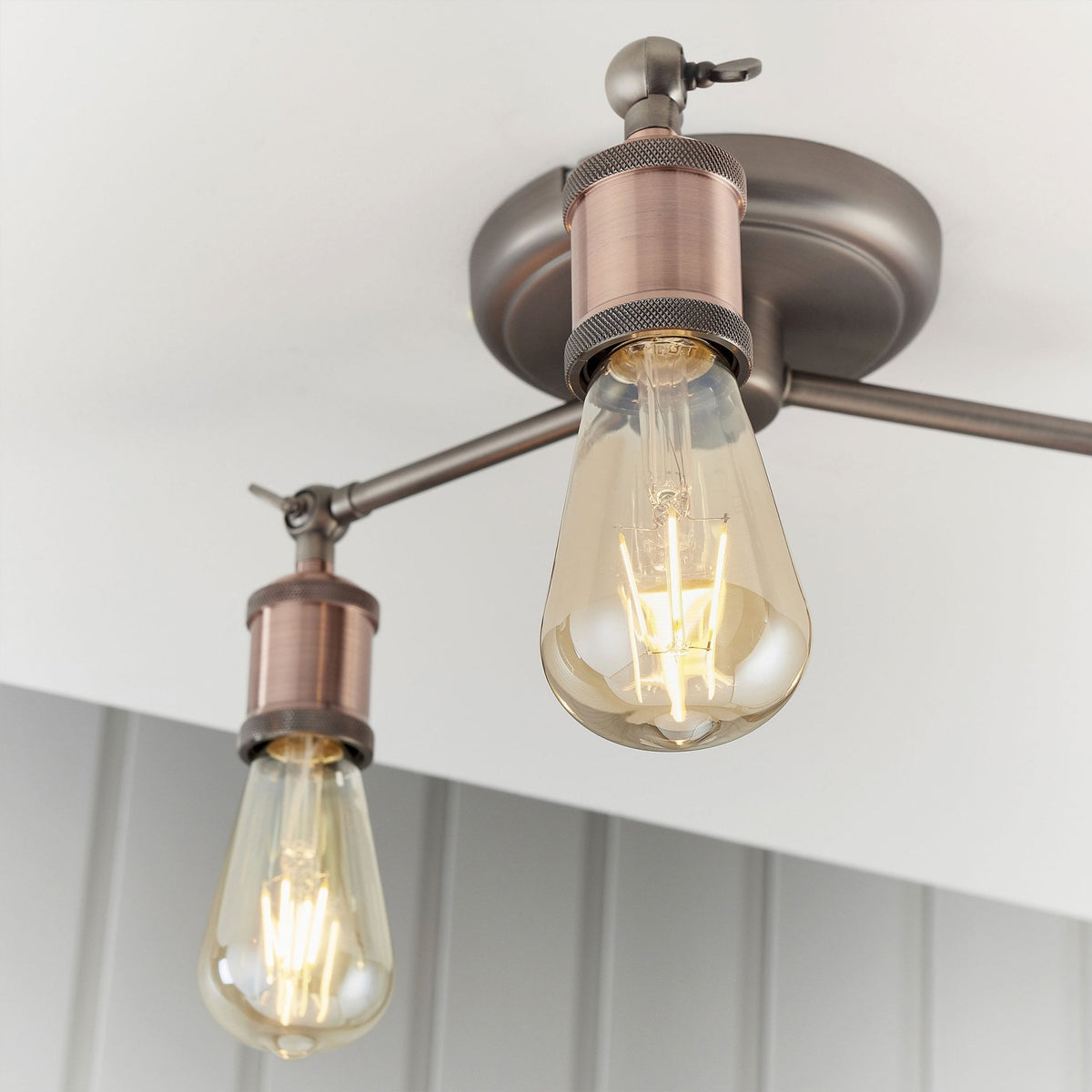 Close-up of two lights on a semi-flush ceiling fixture with antique copper bulb holders and exposed bulbs.