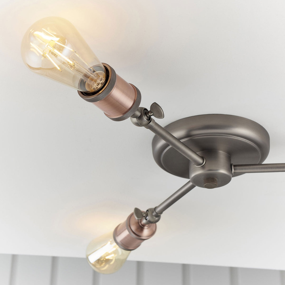 Close-up of two lights on a semi-flush ceiling fixture, one angled upwards with an exposed bulb.