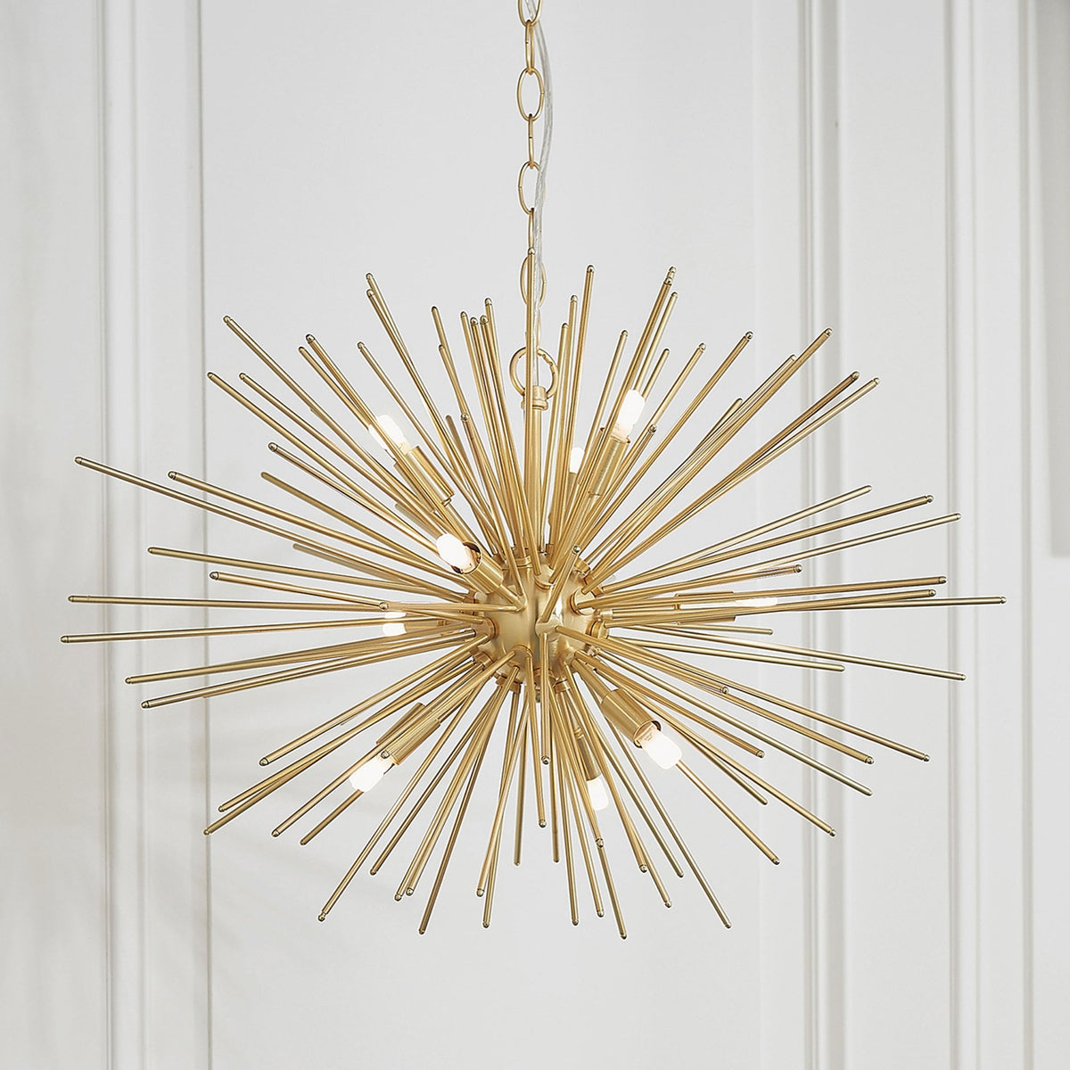 Gold sputnik chandelier with multiple light bulbs, hanging against a white paneled wall.