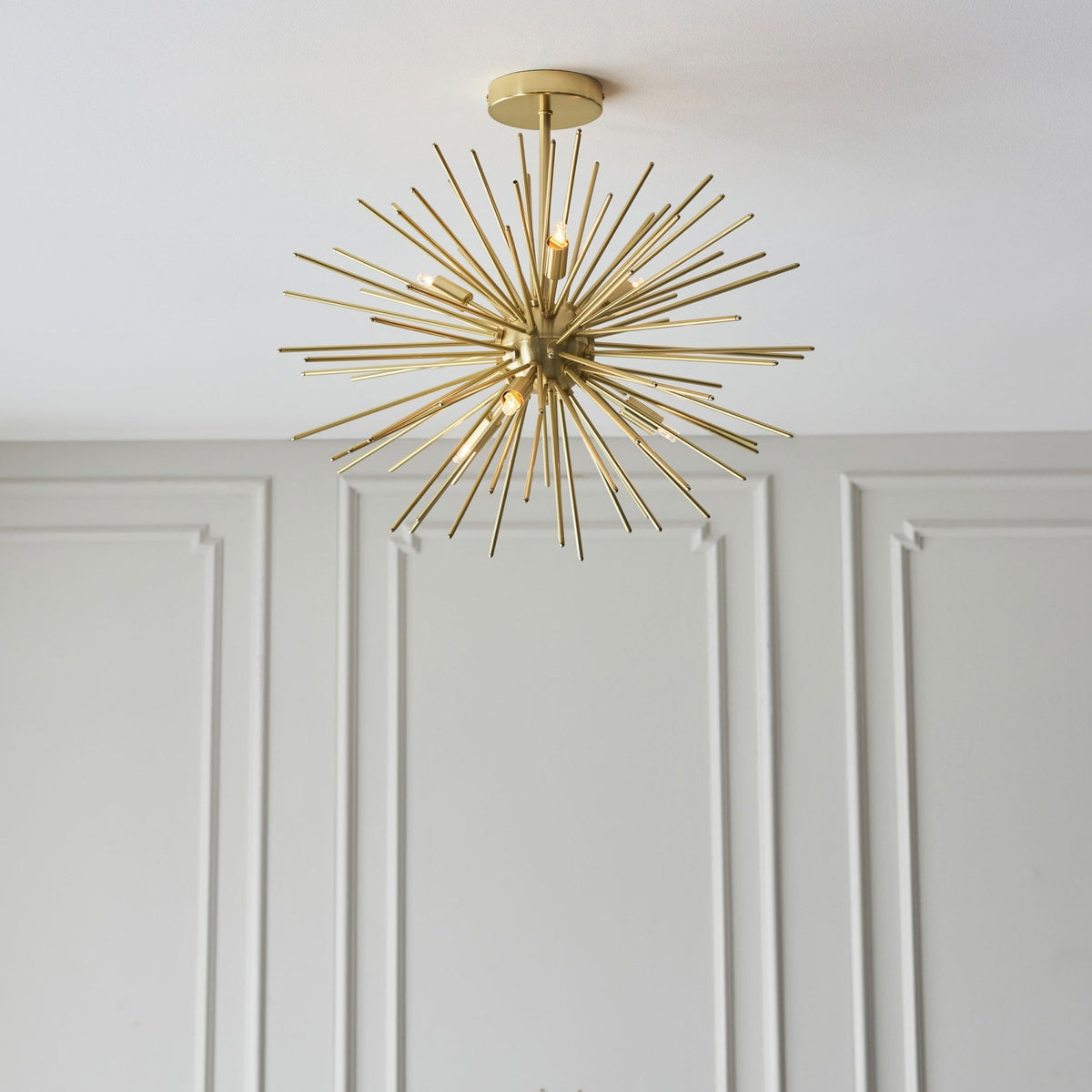 The Sputnik chandelier mounted on a ceiling, illuminating a room with elegant white wall paneling.