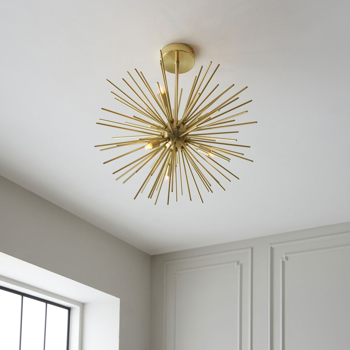The gold Sputnik chandelier in a room corner with a window, showcasing its bright ambiance.
