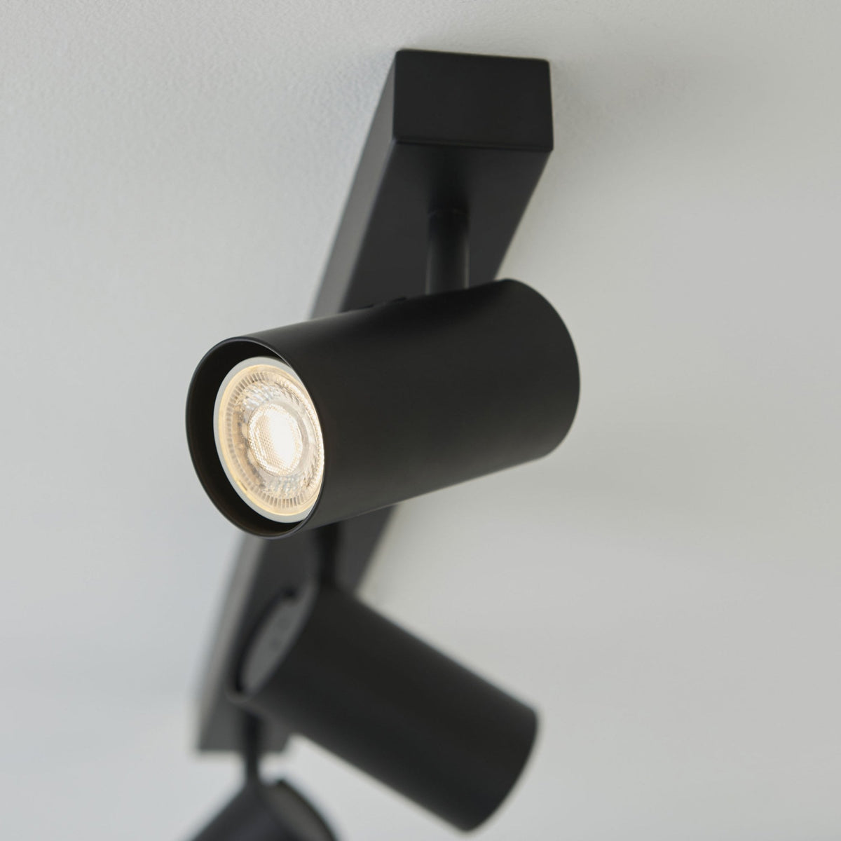 A close-up of a black, cylindrical spotlight from a track light, showing its illuminated bulb.
