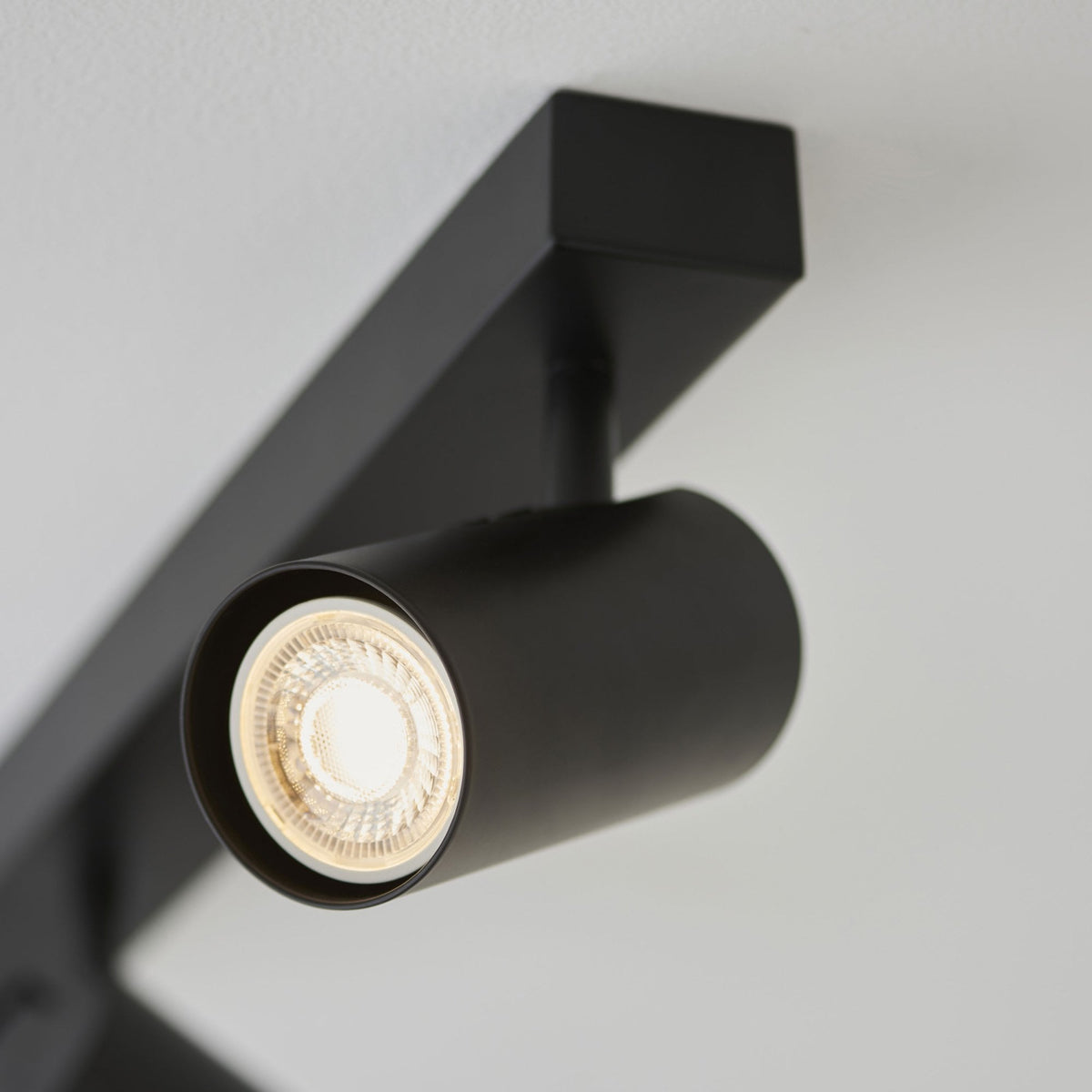 A close-up view of a single illuminated black spotlight on a track light fixture against a white ceiling.