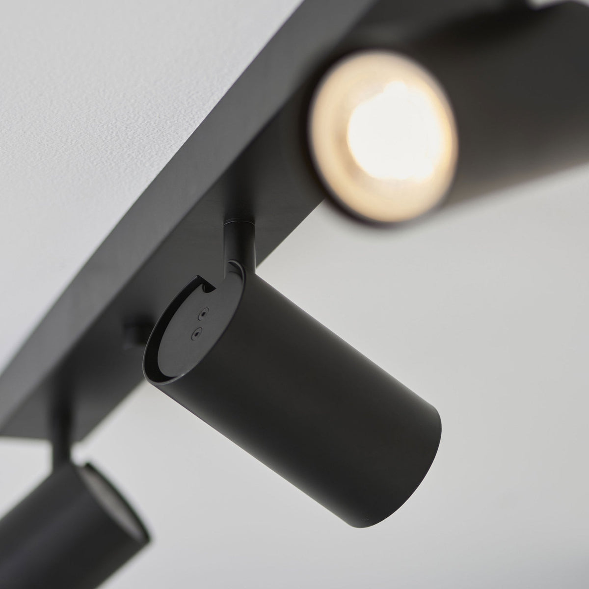 Two black spotlights on a track light, with one illuminated, against a bright white background.