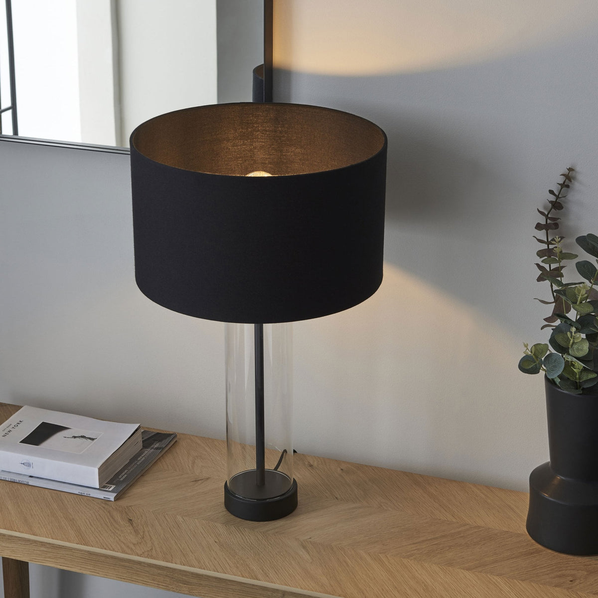 A black table lamp with a cylindrical glass base and a visible light bulb, showcasing its modern design.