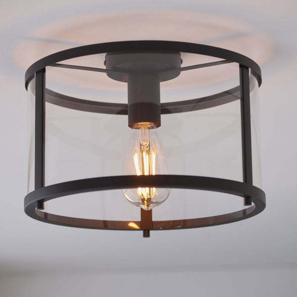 Close-up of a flush-mount ceiling light with a black frame, clear glass, and exposed bulb.