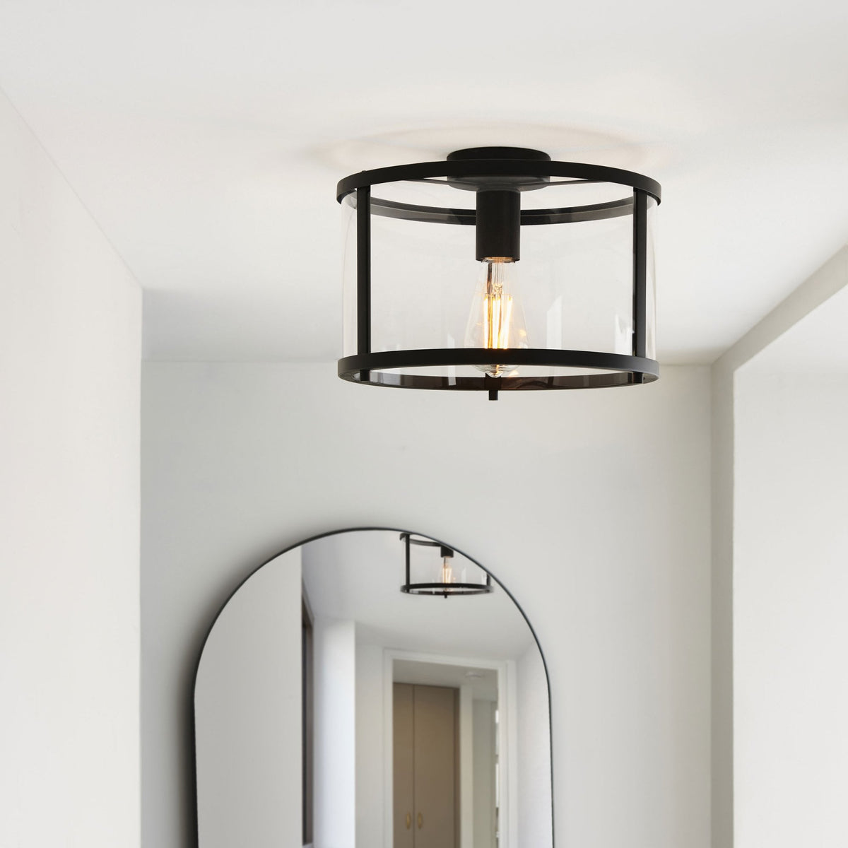 Flush-mount ceiling light illuminating a bright hallway with a minimalist arched mirror.