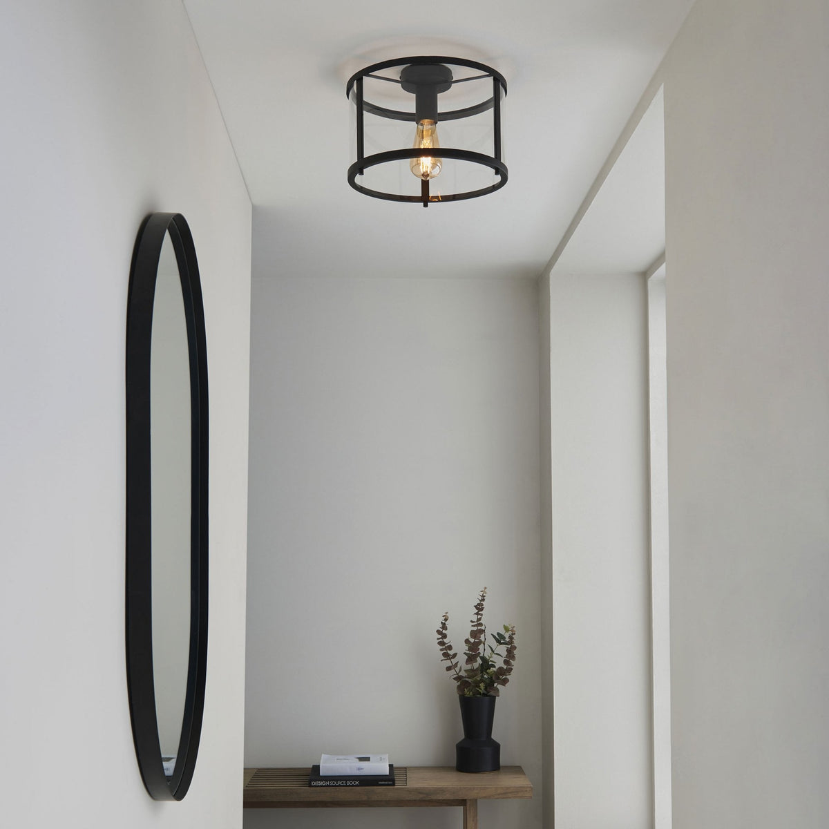 A stylish flush-mount ceiling light in a modern hallway with a tall oval mirror.