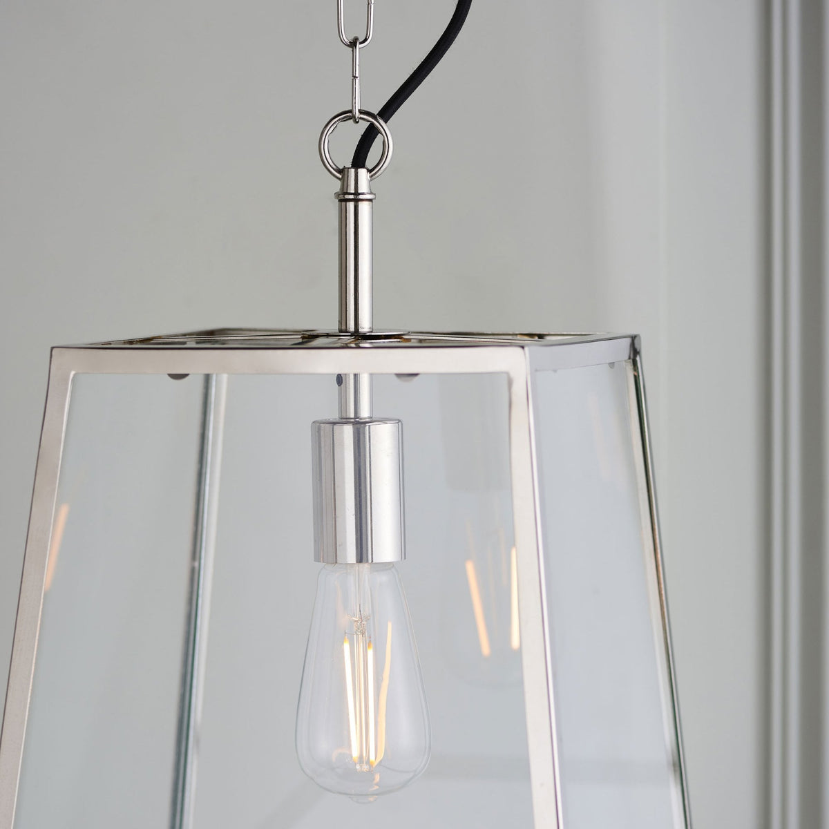 Close-up of a clear glass and metal pendant light with an exposed filament bulb.