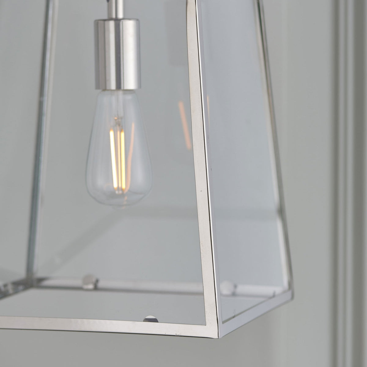 Detail shot of the bottom corner and glass panel of a modern pendant light with a filament bulb.