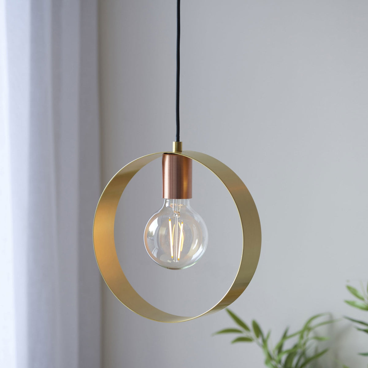 A close-up of a pendant light with a brass ring and copper accent, holding an exposed bulb.