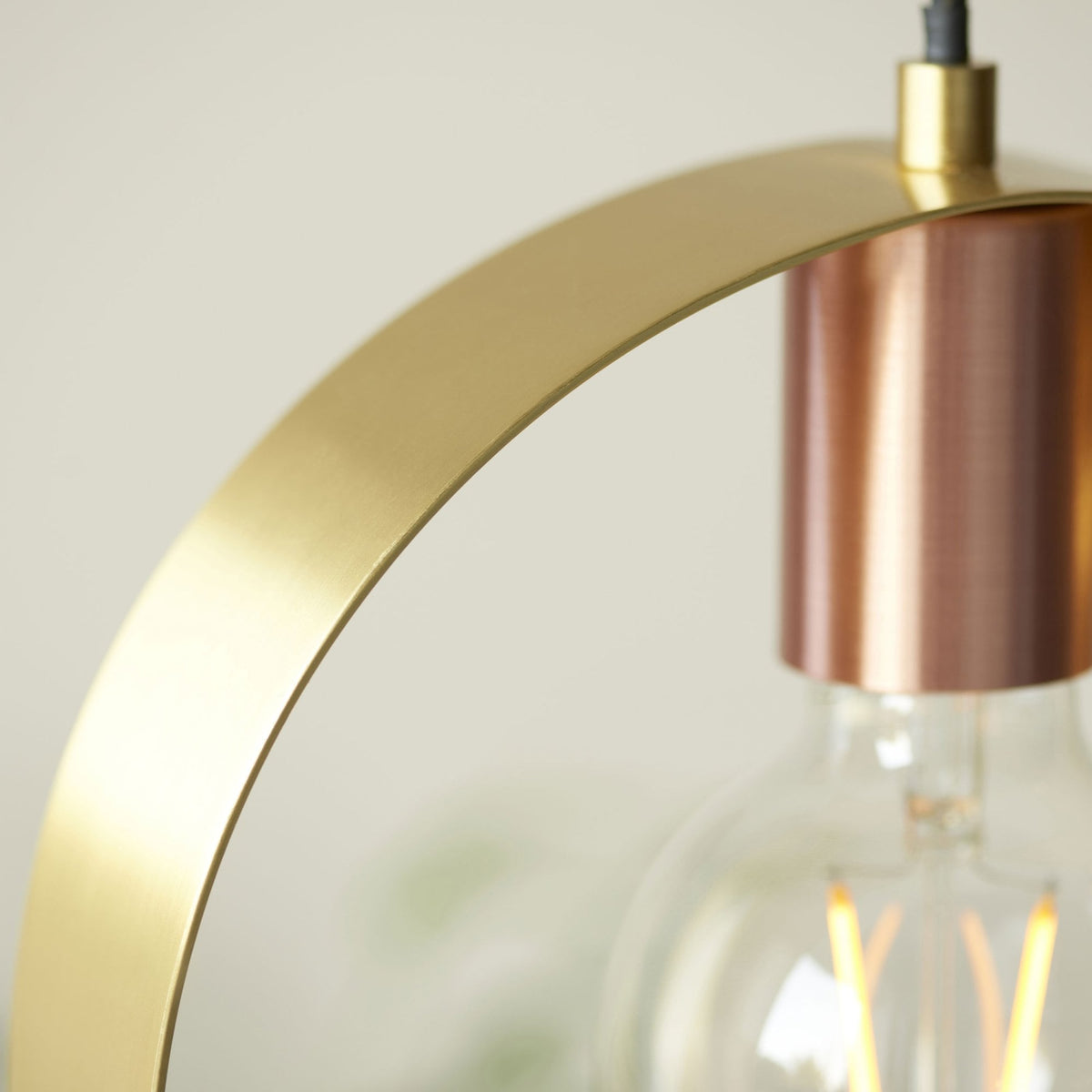 A detailed close-up of the brass ring and copper holder of the pendant light, with a blurred bulb.