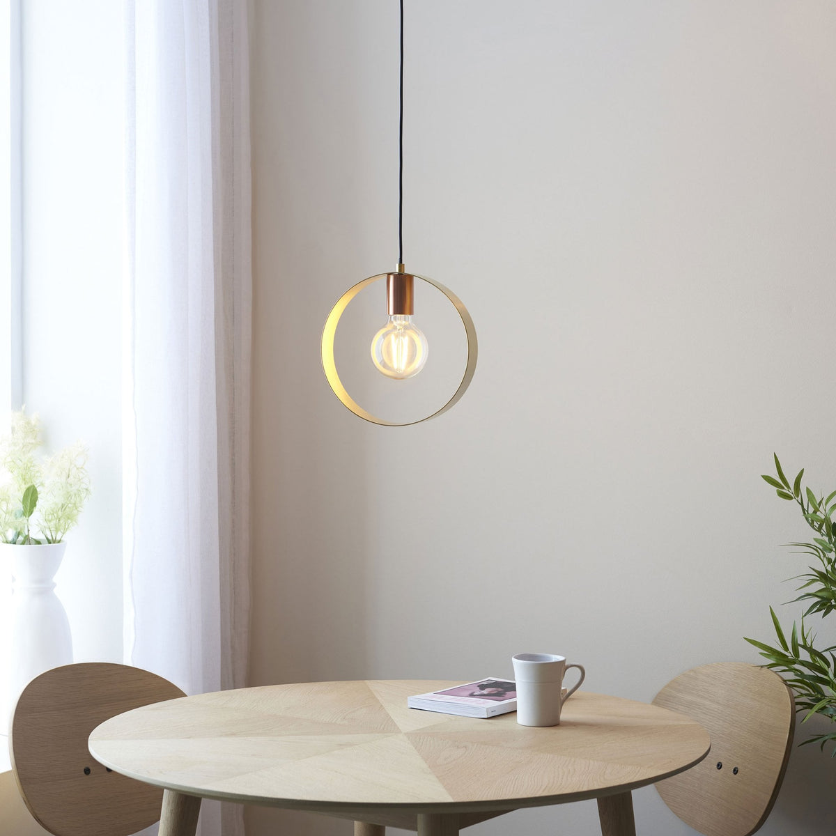 The pendant light illuminates a cozy dining area with a round wooden table and chairs by a window.