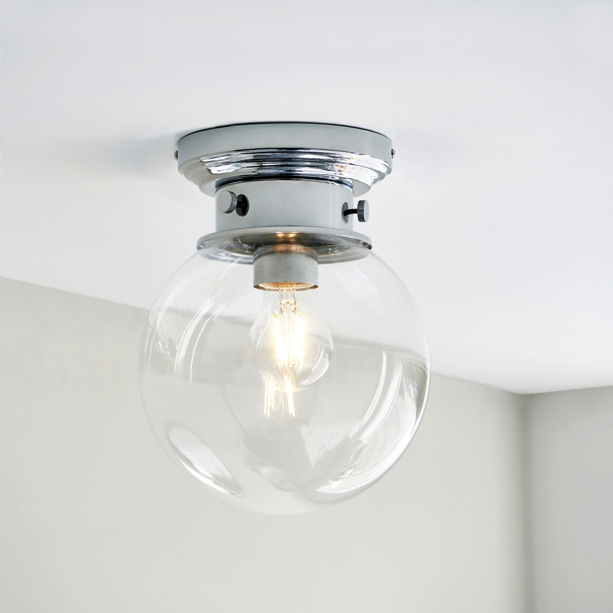 A close-up of a flush mount ceiling light with a clear glass globe and chrome base.