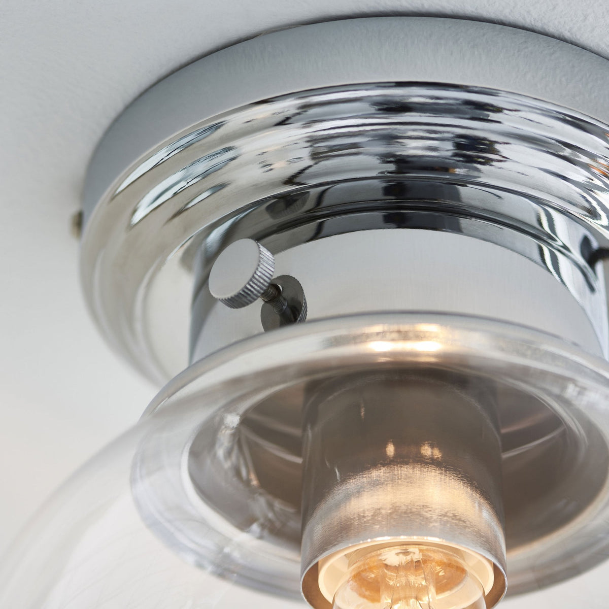Close-up of the chrome base and bulb of a flush mount ceiling light fixture.