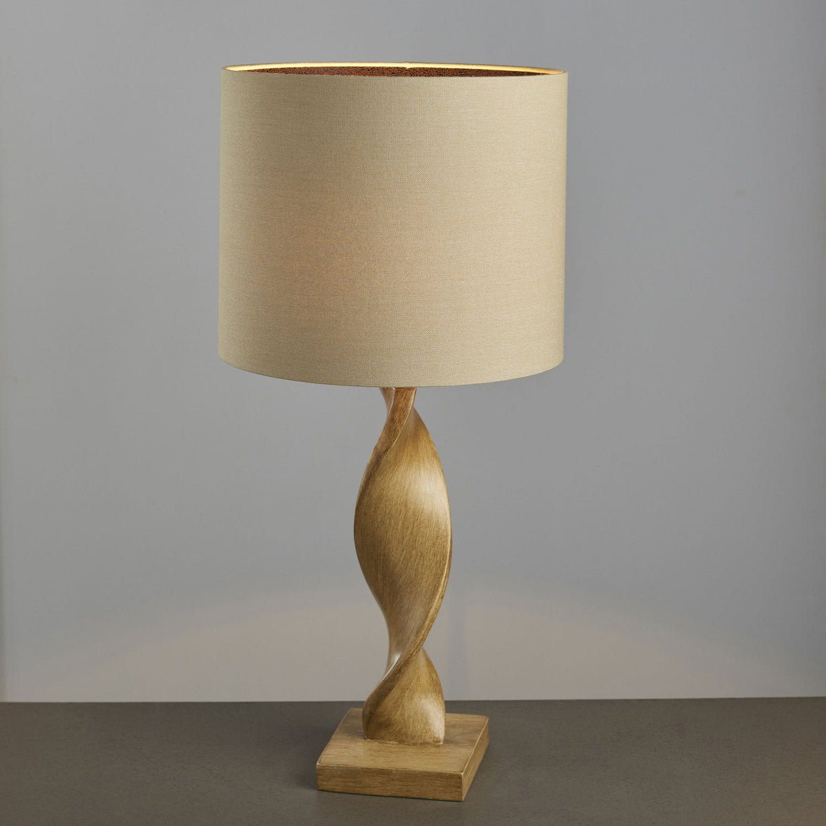 A close-up shot of the tall, twisting wooden base of a modern table lamp with a light-colored shade.