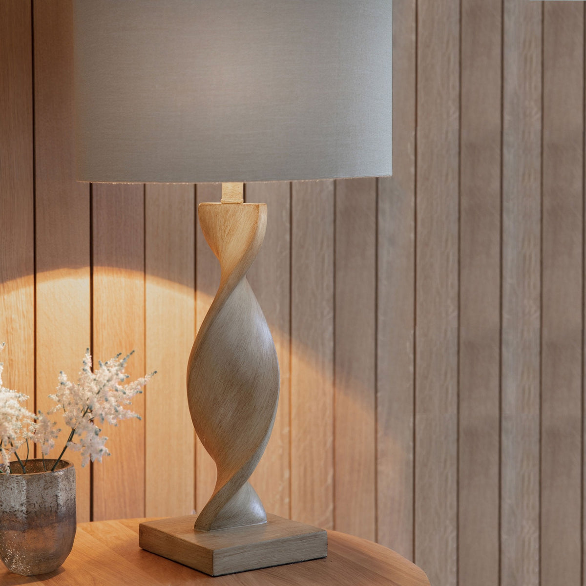 A tall, elegant table lamp with a natural wood twisted base and a neutral fabric shade, casting a warm glow.
