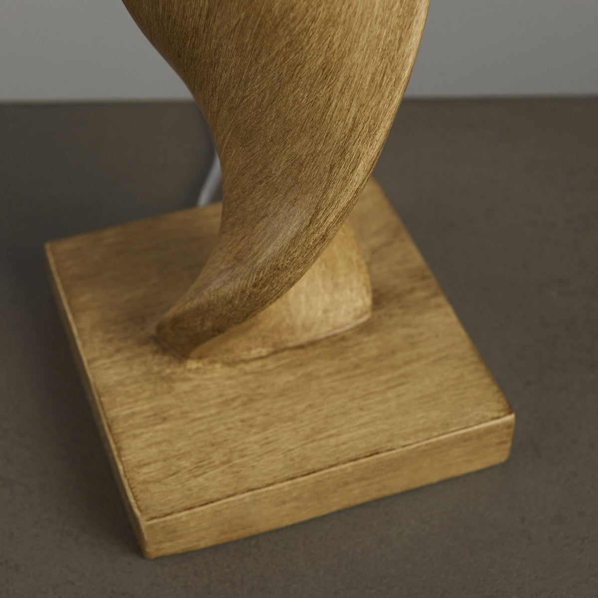 A detailed view of the lamp's square wooden base and the lower part of its unique twisted body.