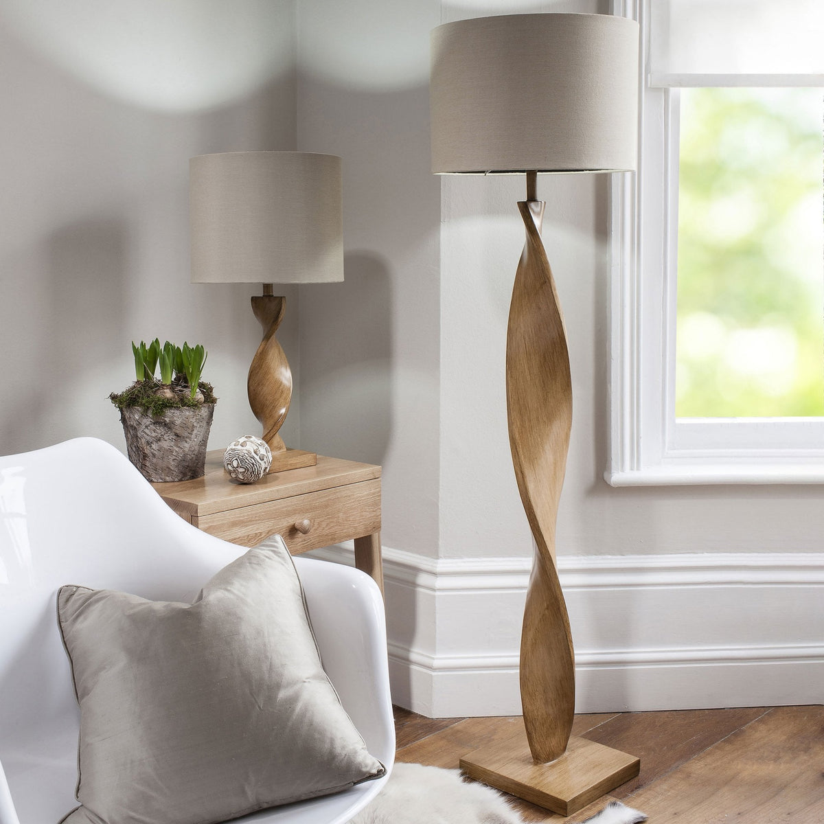 A living room scene featuring a twisted wood floor lamp and a matching table lamp next to a white armchair.
