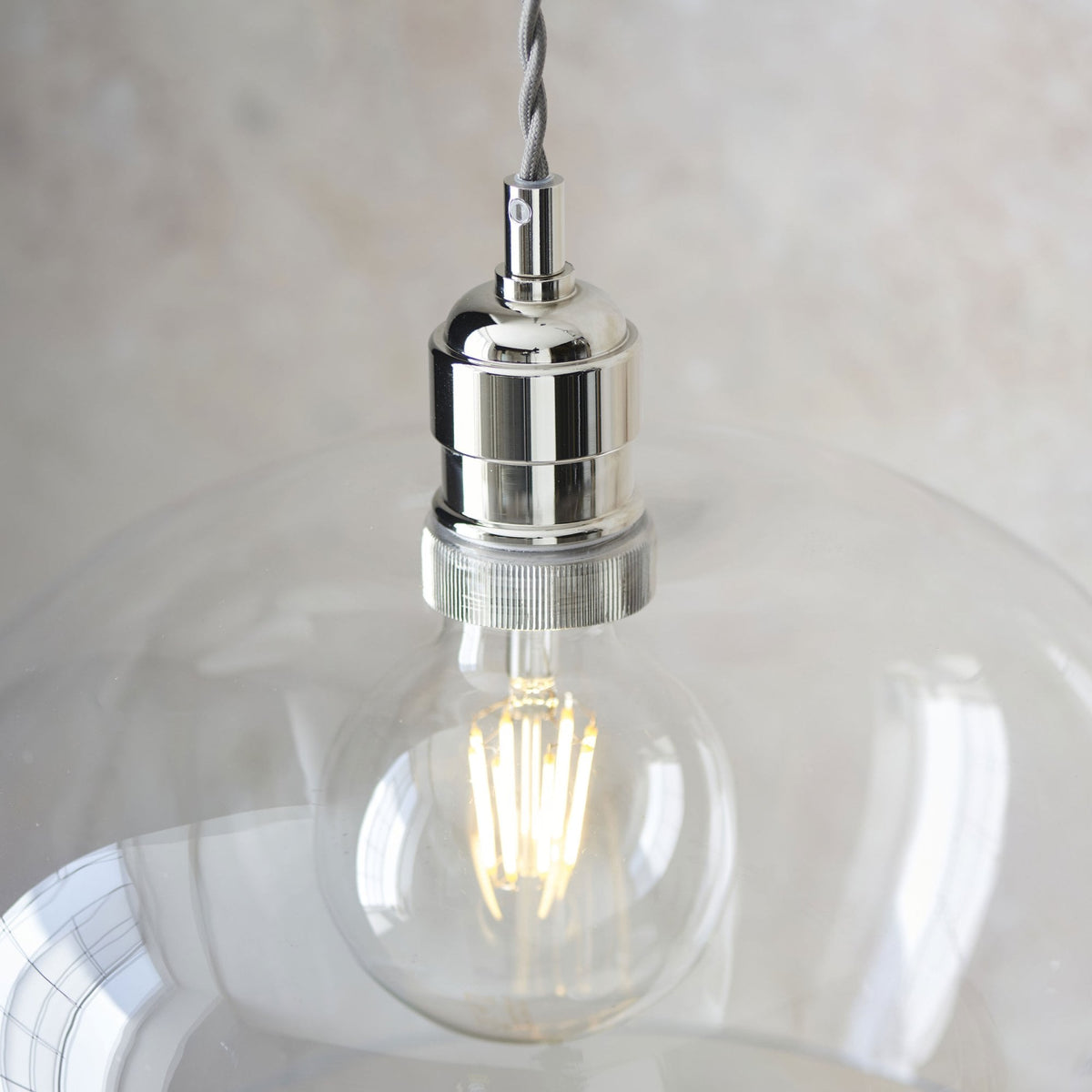 Close-up of a clear glass pendant light showcasing the bulb and polished nickel fitting.