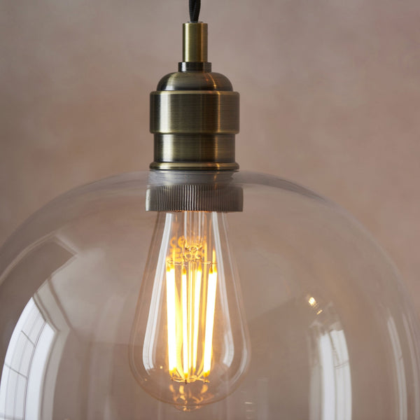 Close-up of a clear glass pendant light with an Edison bulb and antique brass fitting.