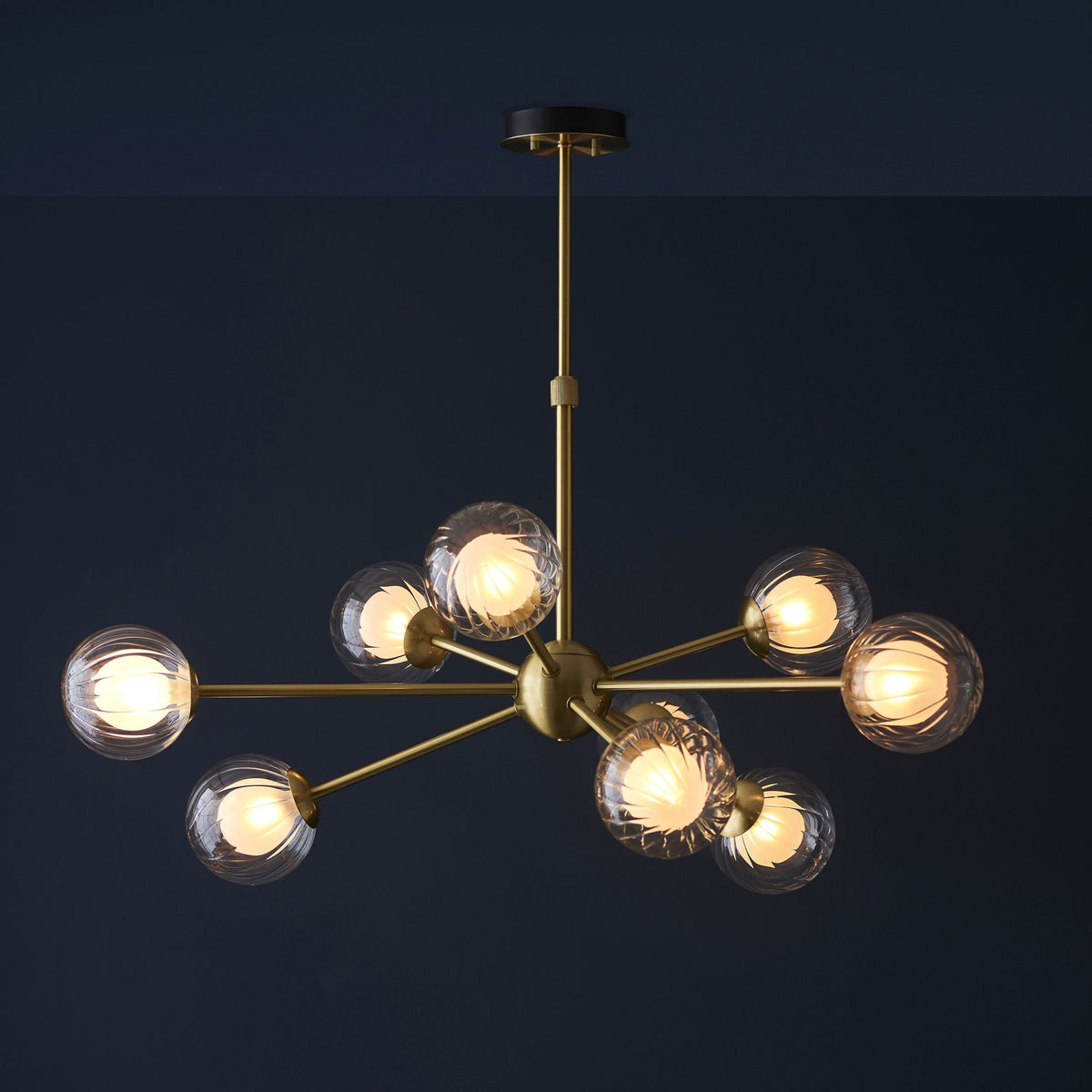 A modern brass chandelier with ten clear, textured glass globe lights illuminated against a dark blue background.