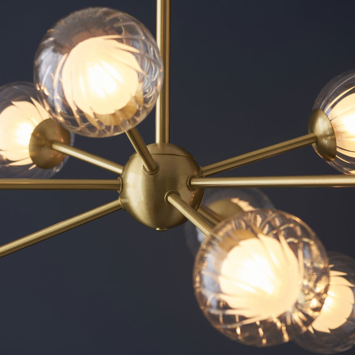Close-up of the brass frame and clear, textured glass globe lights of a modern chandelier.