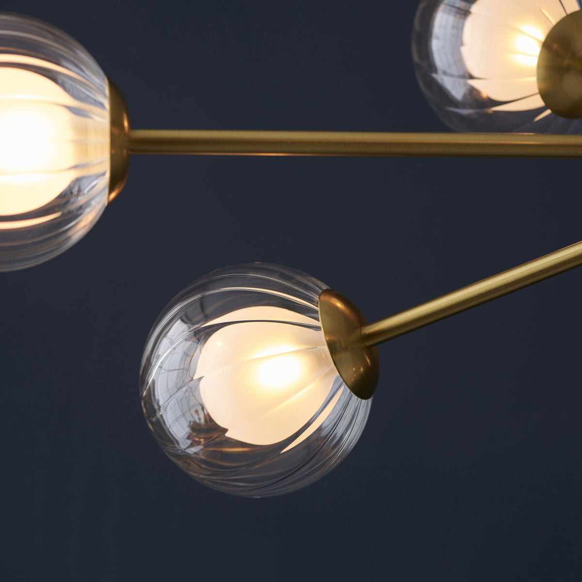 A close-up view of two clear, textured glass globe lights on a brass chandelier against a dark background.