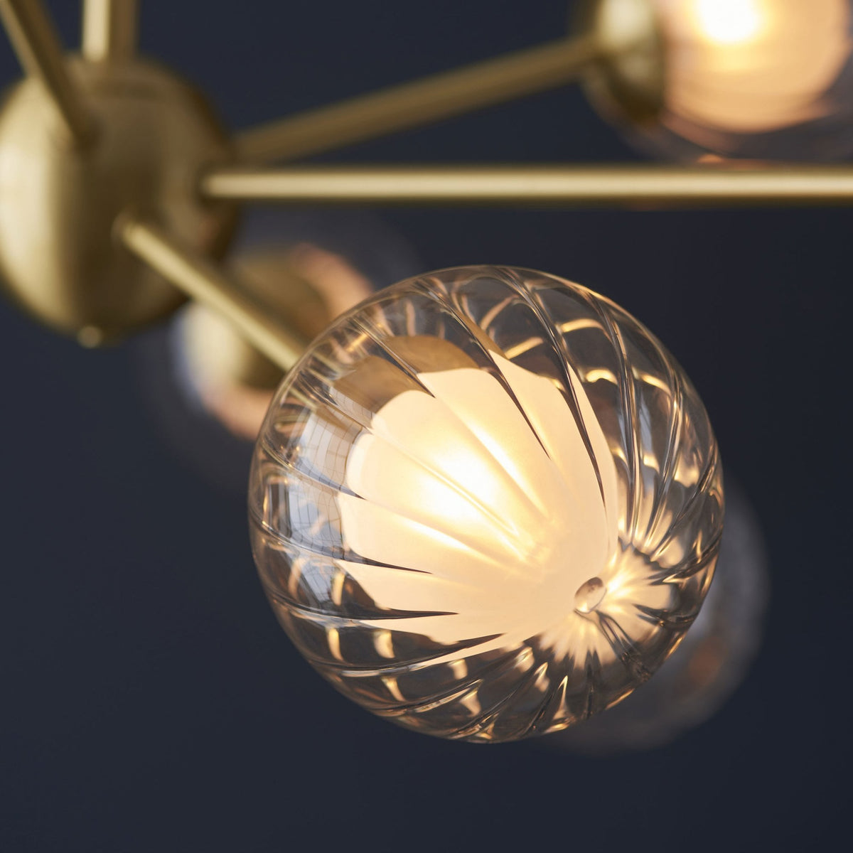A detailed shot of a single clear, textured glass globe light from a brass chandelier.