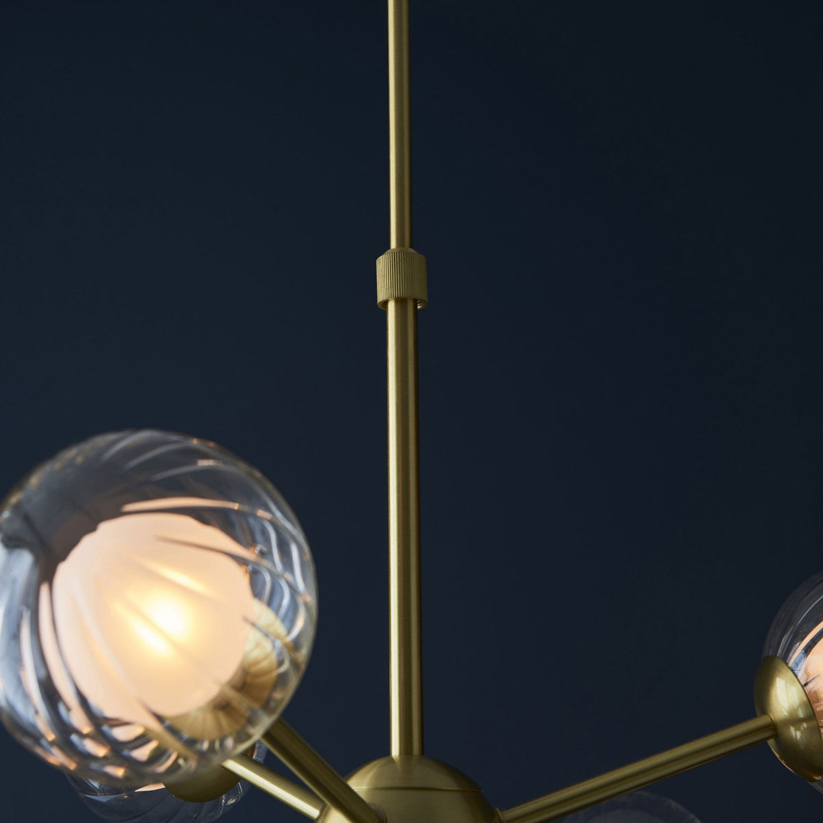 A close-up of the brass stem and clear, textured glass globe lights of a modern chandelier.