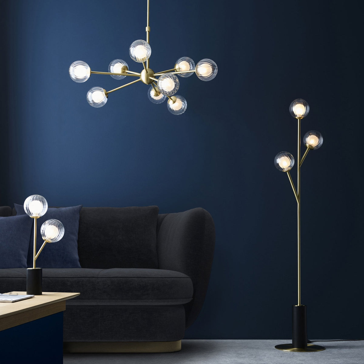 A chandelier, floor lamp, and table lamp, all with clear glass globes and brass bases, in a modern room.