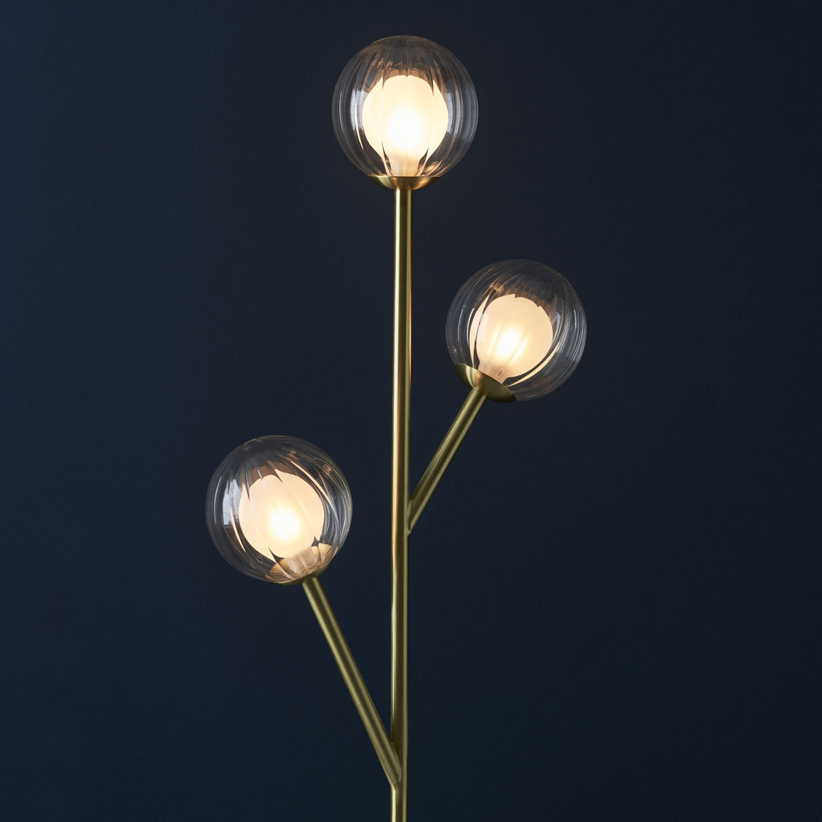 Gros plan sur les trois globes lumineux en verre texturé du lampadaire en laiton, offrant un éclairage d'ambiance.
