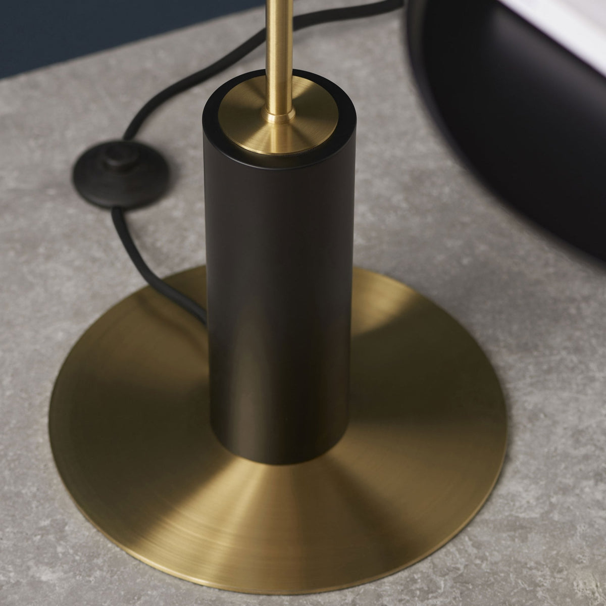 Base du lampadaire, un disque en laiton avec un cylindre noir élégant, sur un sol en béton texturé.