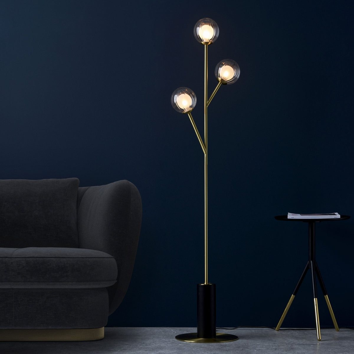 Un lampadaire moderne en laiton avec trois globes lumineux illumine un intérieur élégant aux murs bleu foncé.