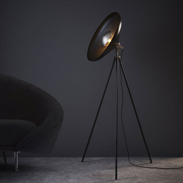 A black tripod floor lamp with a gold inner shade and a dark grey sofa.