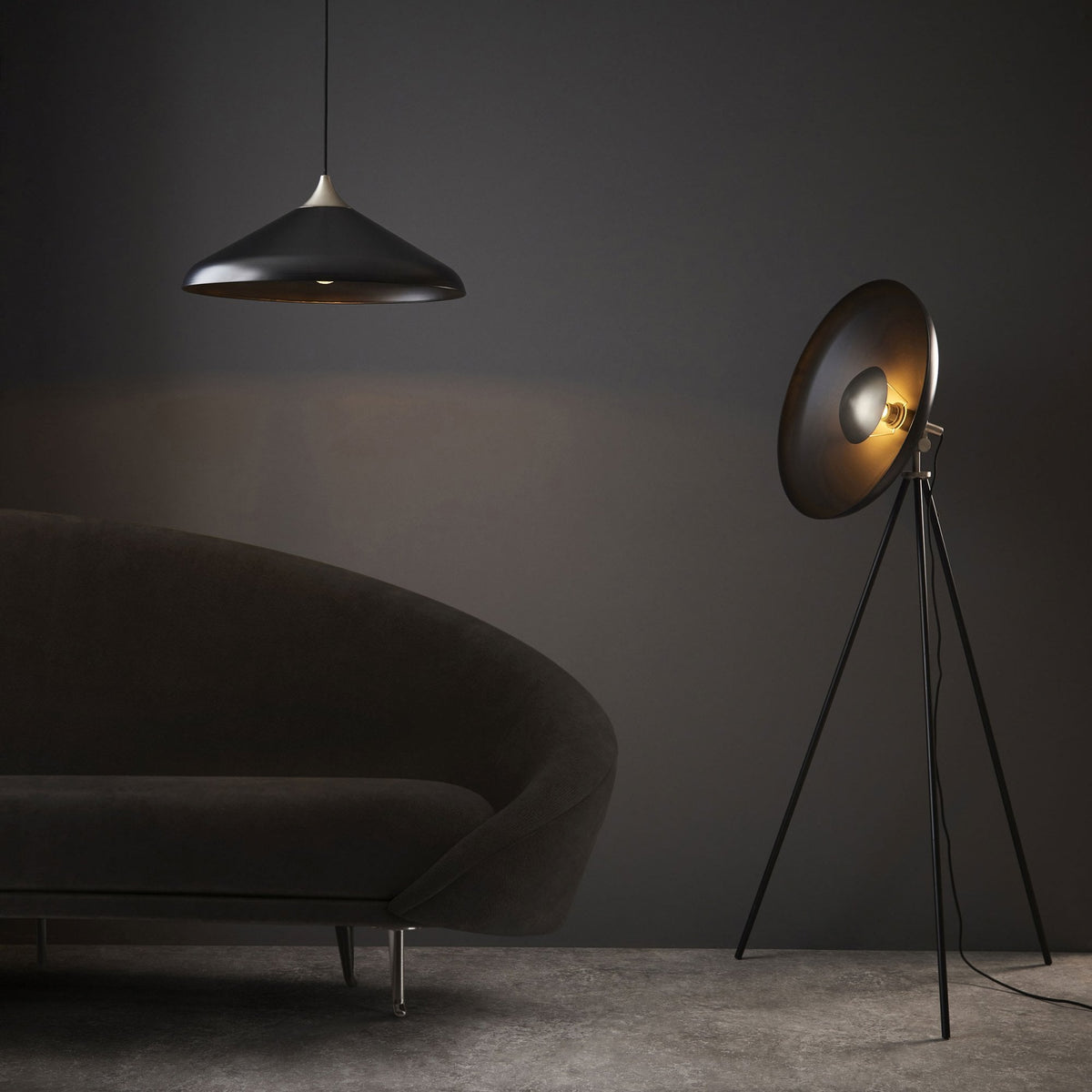 A black tripod floor lamp and a dark grey sofa with a pendant light above.