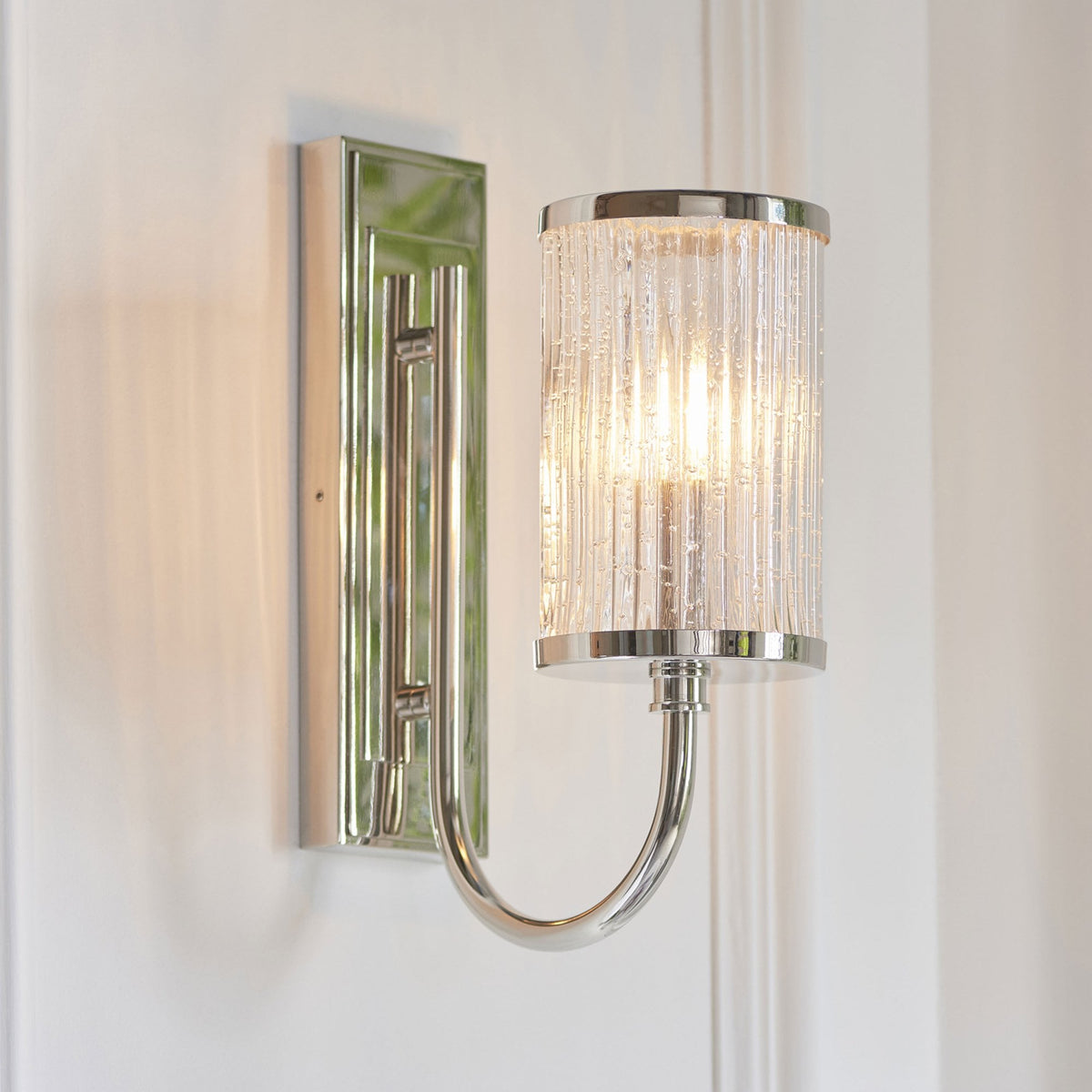 Un aplique de pared de cromo pulido con una pantalla de cristal acanalado burbujeante, iluminado.