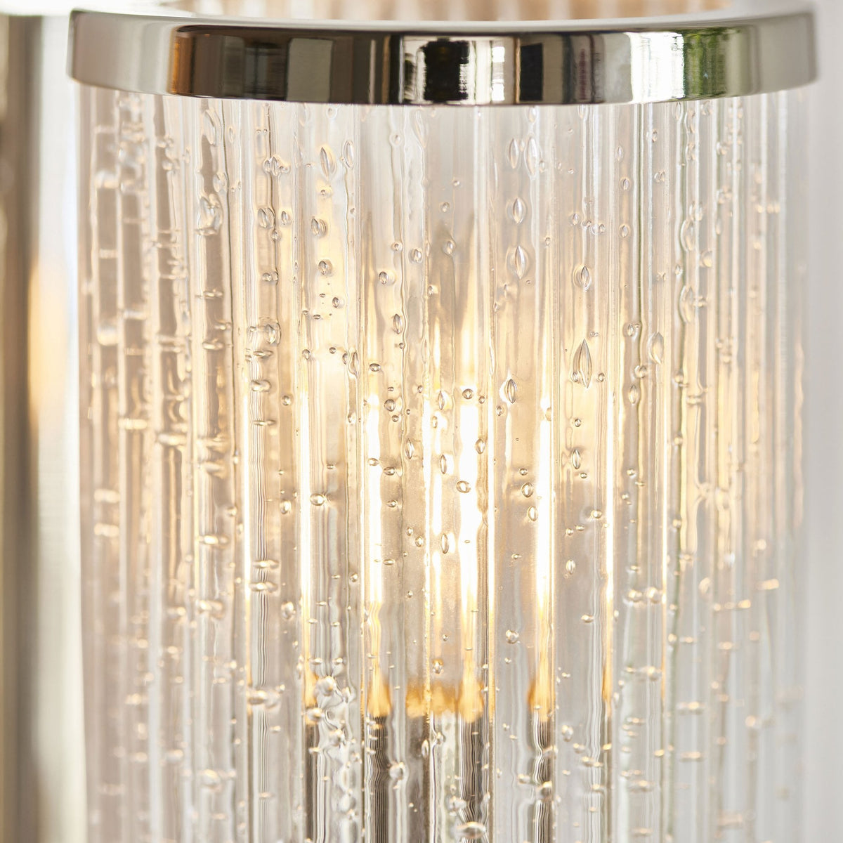Primer plano de un aplique de pared de cromo pulido con una pantalla de cristal acanalado burbujeante, iluminado.