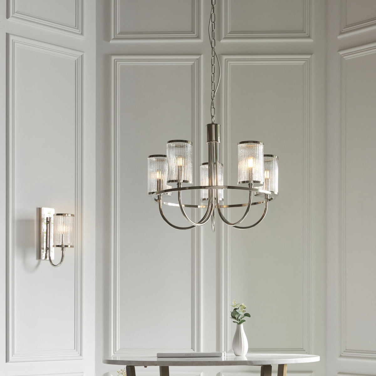 Un candelabro y un aplique de pared a juego de cromo pulido con pantallas de cristal acanalado burbujeante en un entorno de sala de estar.