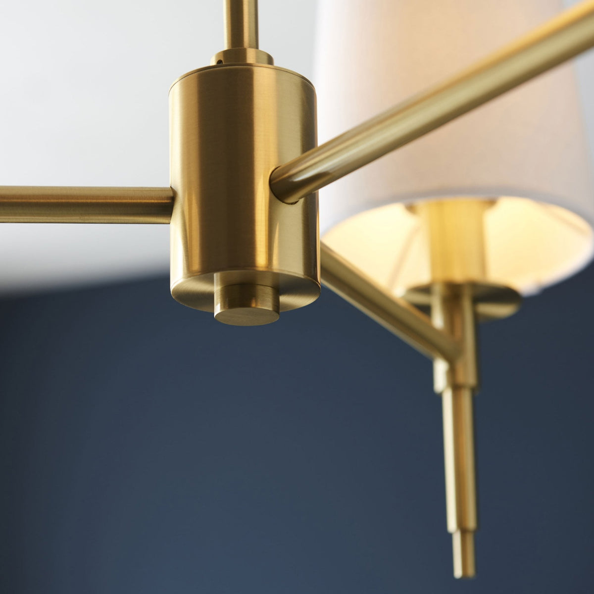 A close up view of the gold-colored central rod and arms of the three-arm chandelier.