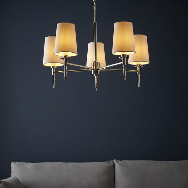 A stylish 5-arm chandelier with cream shades illuminated, complementing a dark blue wall.