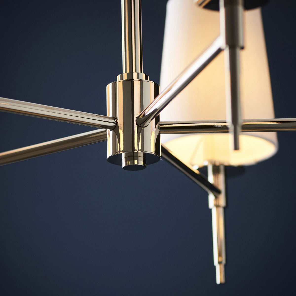 Detail of the polished nickel frame and white fabric shade of a modern chandelier.