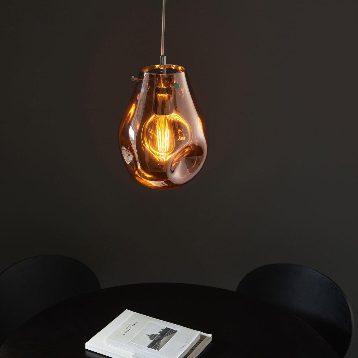 An amber-tinted glass pendant light illuminating a dark table with a book.
