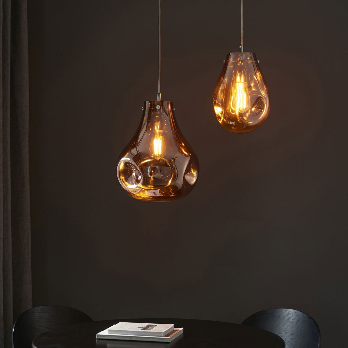 Two amber-tinted glass pendant lights hanging over a dark dining table.
